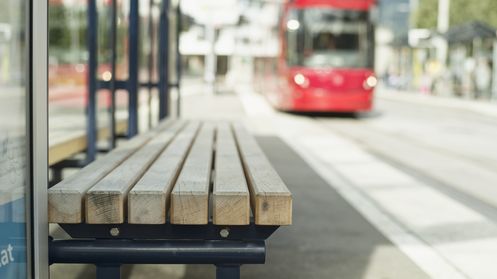 Auf dem Bild ist eine Haltestelle und im Hintergrund eine Tram zu sehen. 